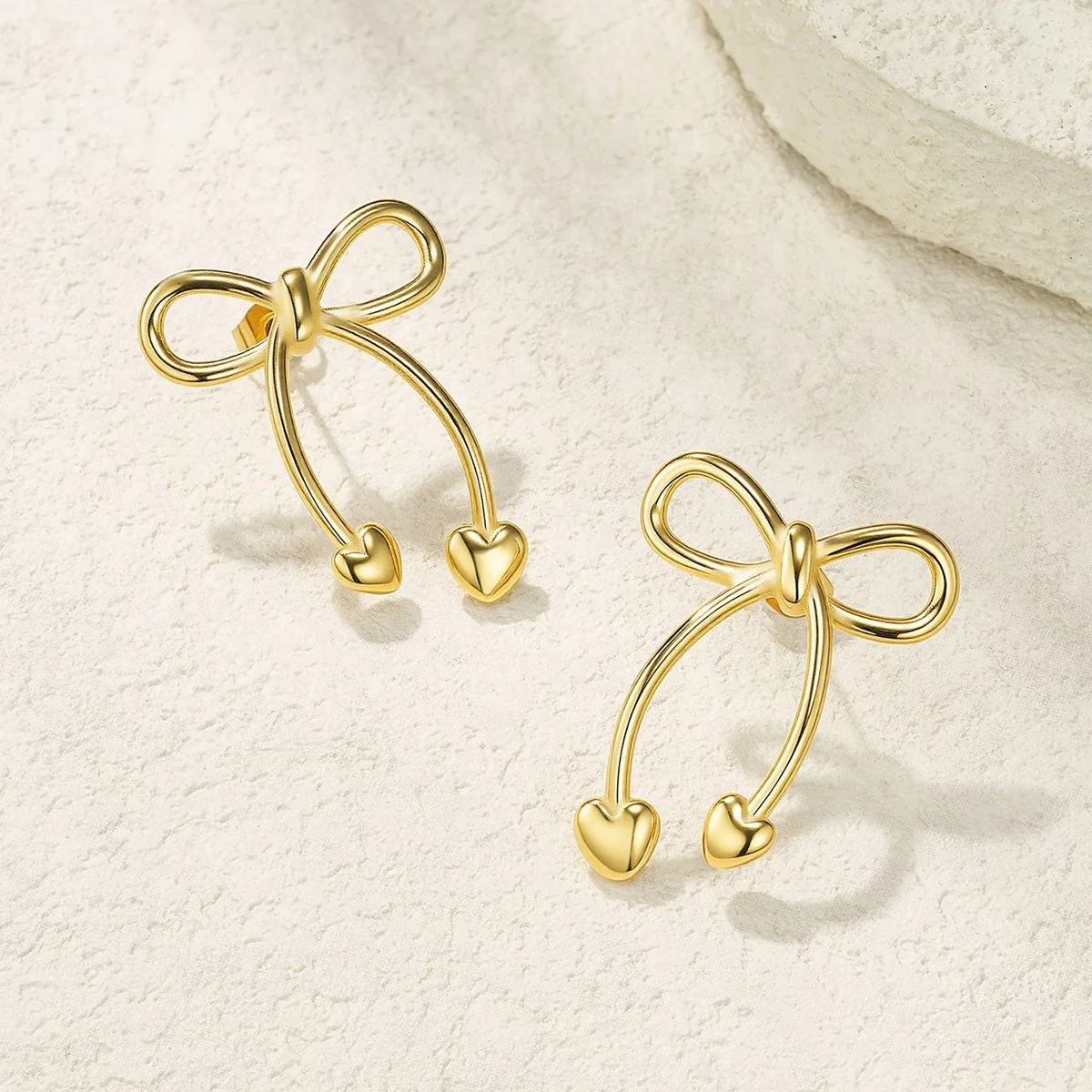 Gold stainless steel bow heart earrings on white background