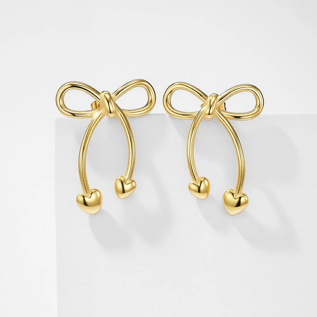 Gold stainless steel bow heart earrings on white background