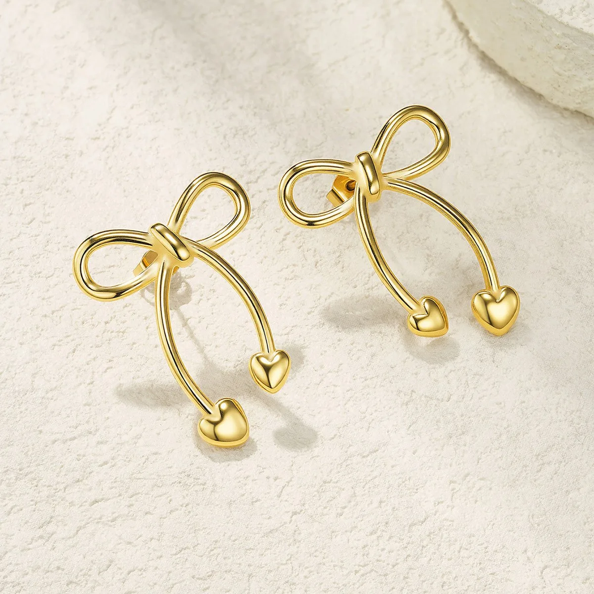 Gold stainless steel bow heart earrings on white background